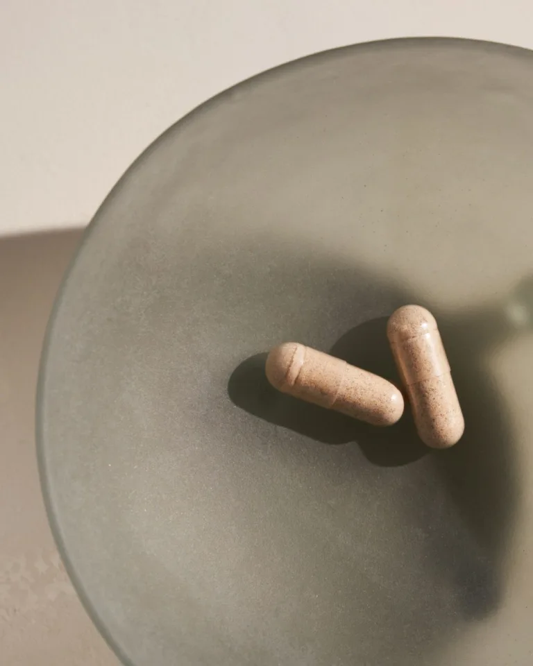 sakara.momplete Probiotic Formula capsules shown close-up on a matte green dish with soft natural lighting.
