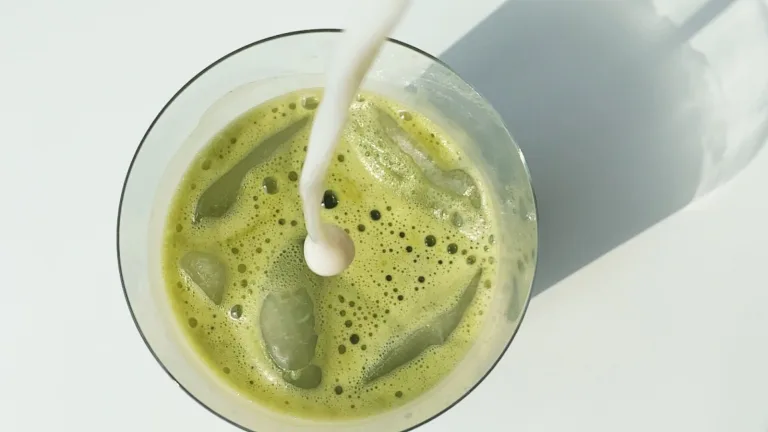 Iced green matcha latte with milk being poured into the glass.