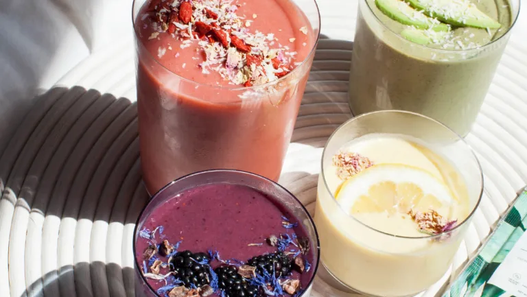 Assorted colorful smoothies in glasses, topped with coconut flakes, fruit, and edible flowers.