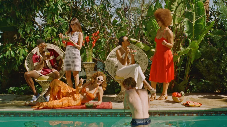 Group of people gathered by a pool surrounded by lush greenery and fresh food.