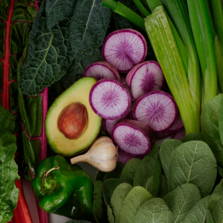 Assorted vegetables including sliced watermelon radishes, halved avocado, green bell pepper, garlic bulb, celery stalks, and leafy greens.
