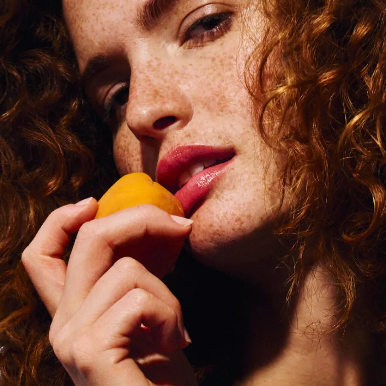 Close-up portrait of a person holding a small orange fruit near their lips.