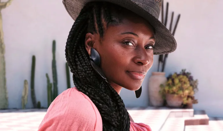 Portrait of Fatima Robinson wearing a wide-brim hat and statement earrings outdoors near desert plants.