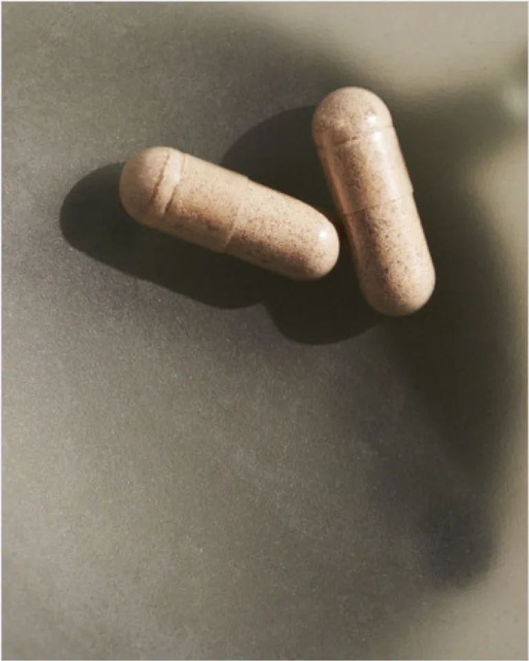 sakara.momplete Probiotic Formula capsules shown close-up on a matte green dish with soft natural lighting.