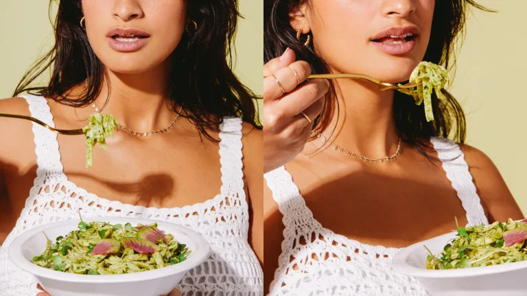 Woman eating a bowl of pasta with pesto and watermelon radishes against a green-toned background.