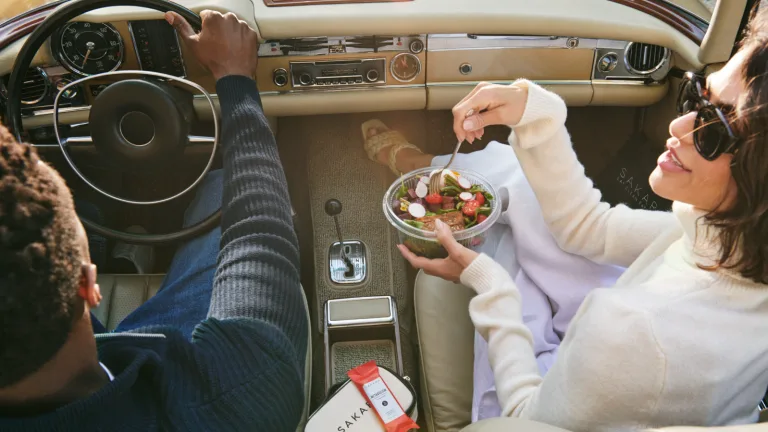 Overhead shot of a man and woman in a car holding a Sakara salad.