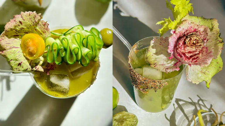 Two cocktail green juices in glasses garnished with cucumber ribbons and leafy greens.