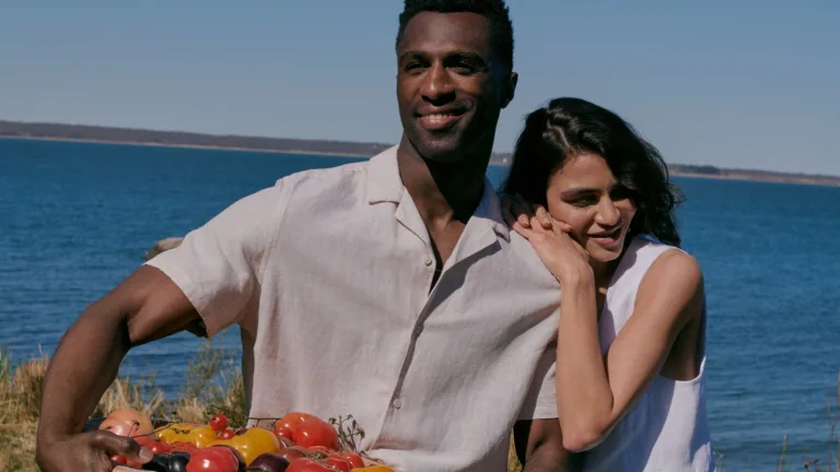 Couple standing by the water with a basket of fresh produce.