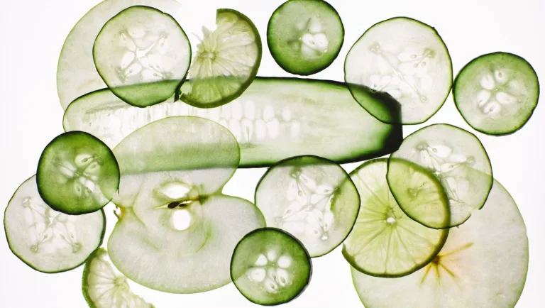 Thinly sliced cucumbers and green apple arranged in overlapping layers on a white background.