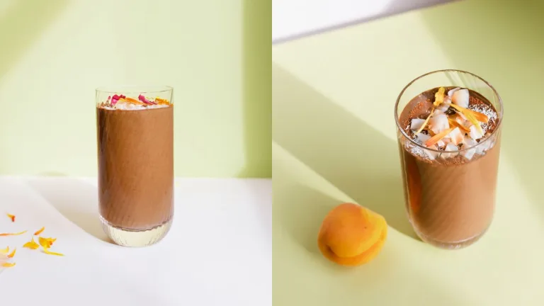 Glass of Metabolism Super Powder chocolate smoothies, topped with coconut flakes, beside a whole apricot.