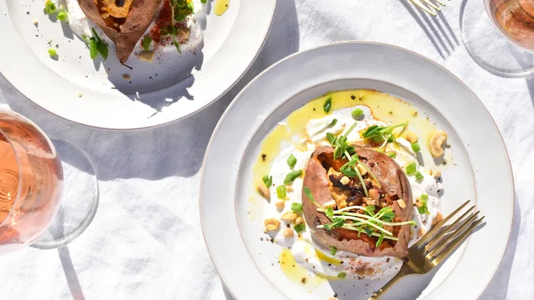 Baked sweet potato topped with yogurt, herbs, and crunchy garnish served on a white plate with olive oil drizzle.