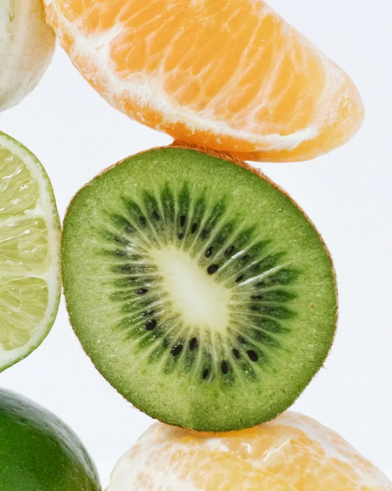Close-up of fresh citrus wedges and a sliced kiwi arranged against a light background.