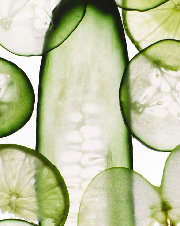 Thinly sliced cucumbers layered on a white background with visible seeds and translucent green edges.