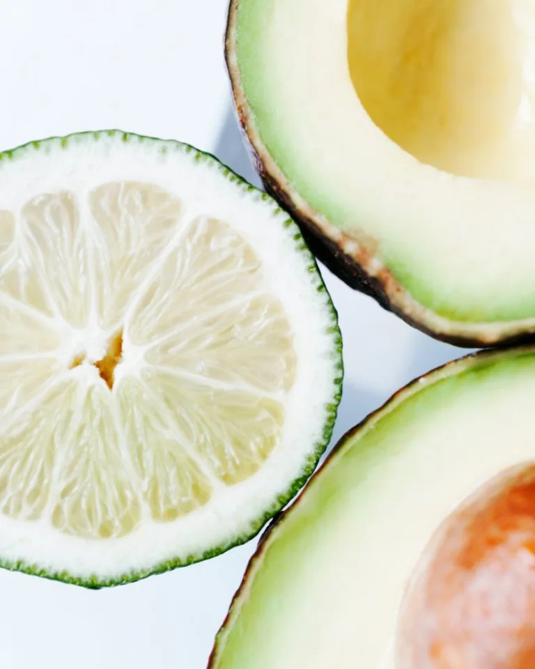 Sliced lime and halved avocado arranged on a light background showing detailed texture and pulp.