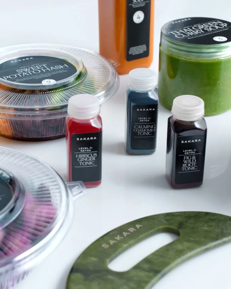 Sakara Level II: Detox assortment featuring Hibiscus Ginger Tonic, Calming Chamomile Tonic, Fig & Wild Root Tonic, Thai Green Curry Soup, Sweet Potato Hash, and a green Sakara-branded body gua sha tool.