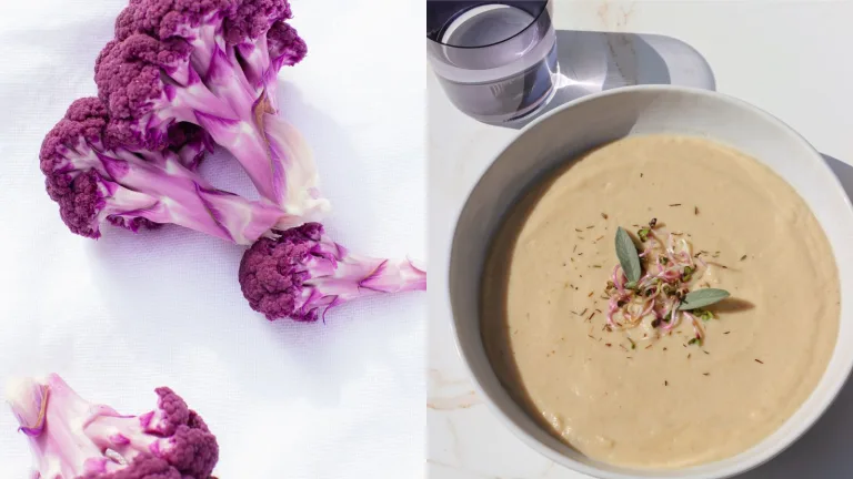 Creamy blended cauliflower soup garnished with herbs and finely sliced vegetables in a white bowl.