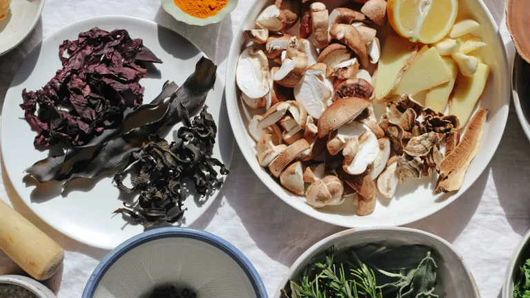 Assorted mushrooms and seaweed arranged on white plates with herbs and lemon nearby.