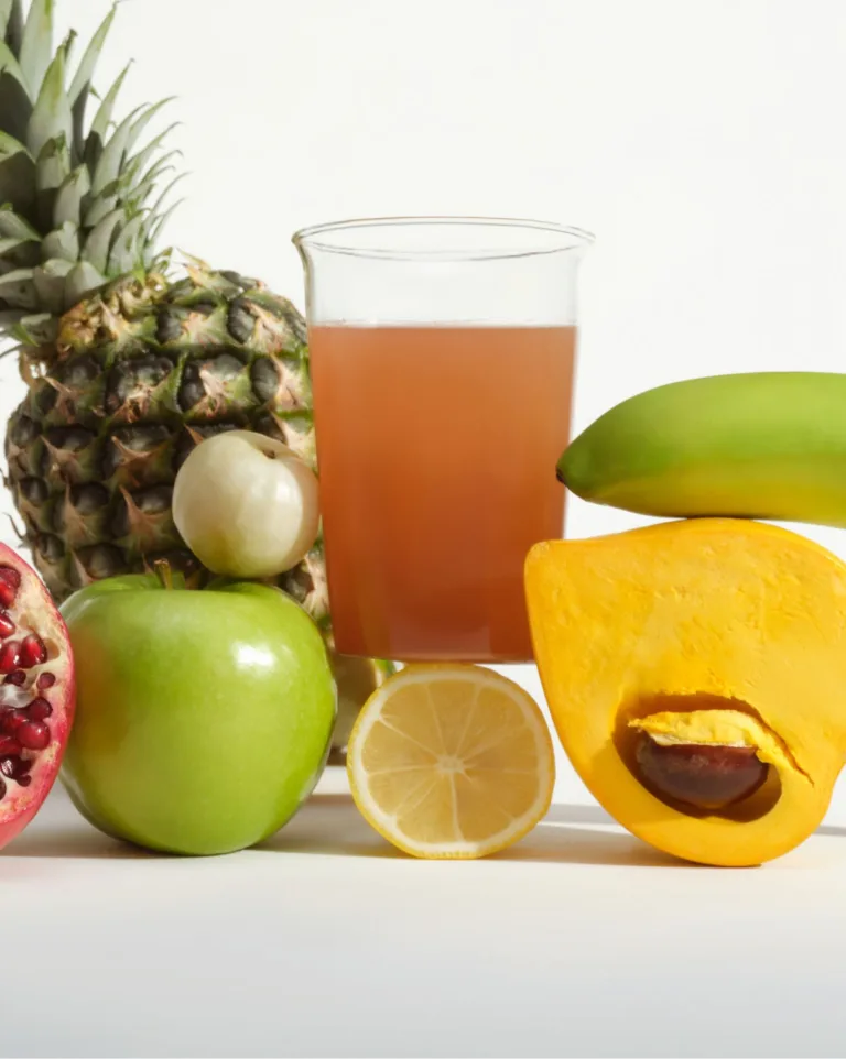 Sakara Fiber Super Powder mixed in water alongside produce including pineapple, pomegranate, green apple, lemon, and green banana on white studio background