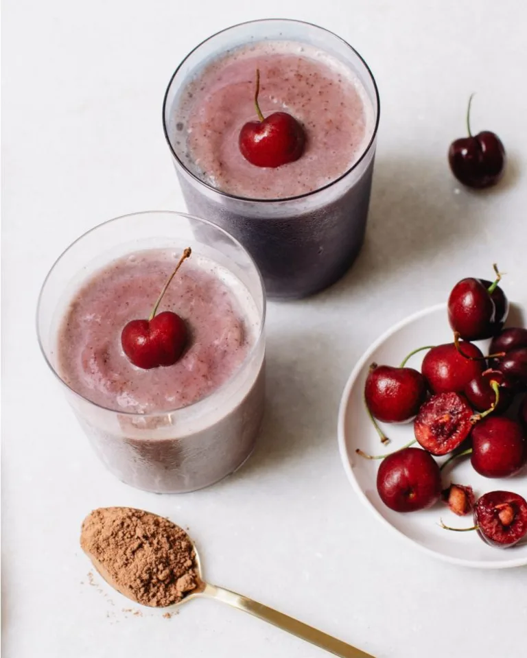 Chocolate-Cherry Metabolism Super Powder Smoothie in two glasses topped with cherries, sitting next to a bowl of cherries.