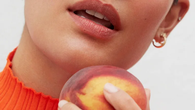 Close-up of a woman holding a peach near her lips.