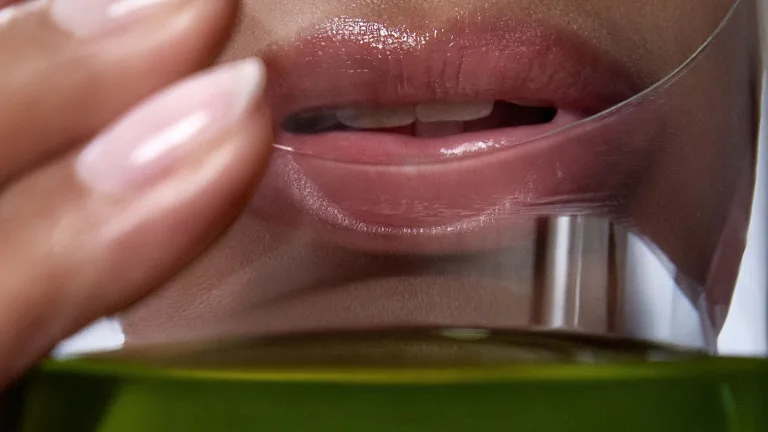 Close-up of a female's lips drinking from a glass container with green Daily Elixir liquid multivitamin.