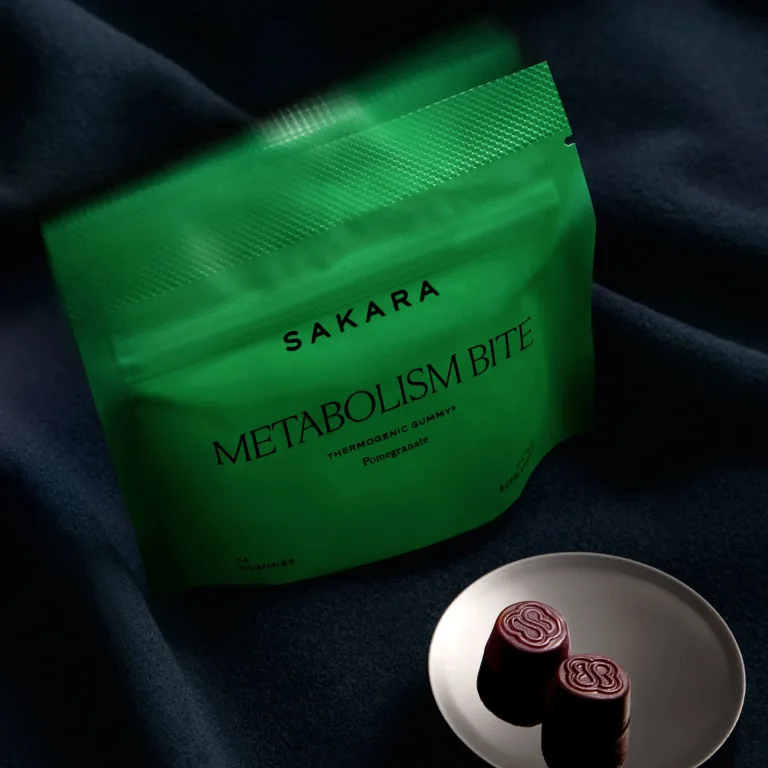 Sakara Metabolism Bite thermogenic gummies in bright green resealable pouch with black text, pomegranate flavor, 14 gummies dietary supplement, shown with two dark red gummies on white plate