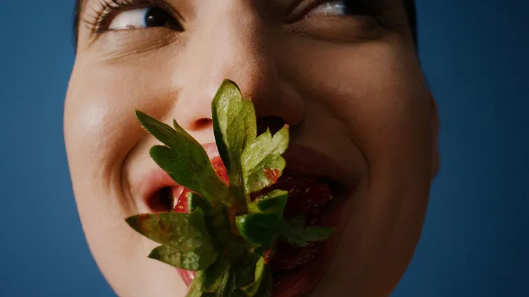 Close-up of a female holding a strawberry near their mouth.