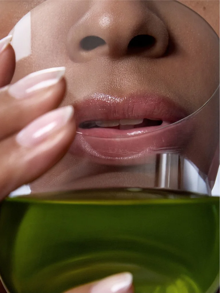 Person drinking green liquid from cup representing Sakara Daily Elixir liquid multivitamin in Lemon Verbena-Mint flavor against neutral studio background