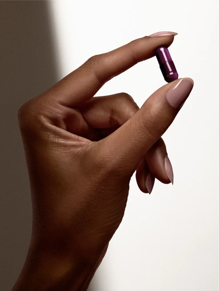 Hand holding purple Sakara Night Service sleep support capsule between fingers against neutral background