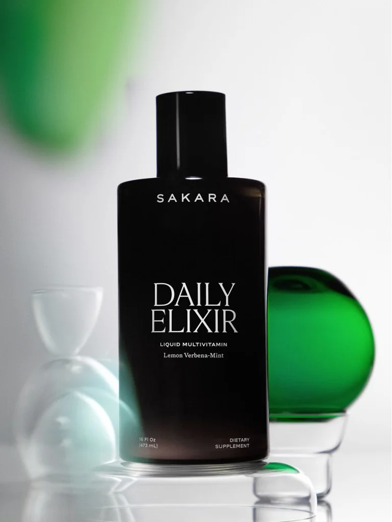 Sakara Daily Elixir in a dark glass bottle with black cap displayed beside a green glass orb on a light background.