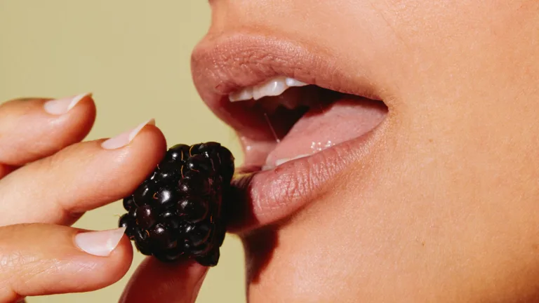 Close-up of a woman's lips holding a blackberry near the mouth.