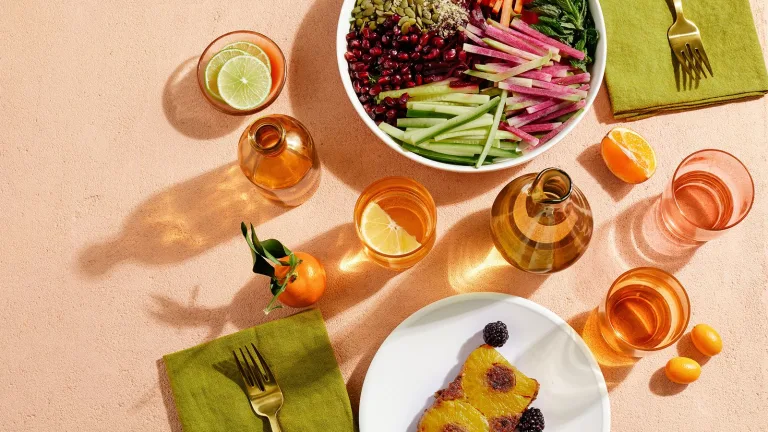 Overhead view of a table setting with colorful salads, citrus slices, glassware, and a plated dessert.