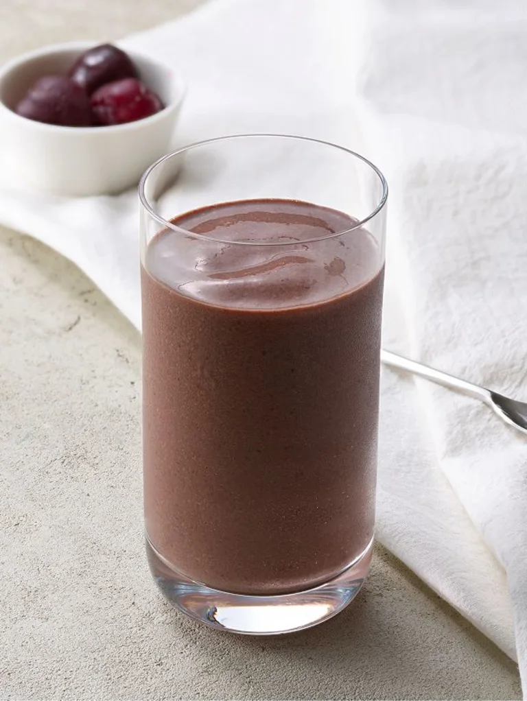 Sakara Metabolism Super Powder blended into a chocolate smoothie in a clear glass, demonstrating blending it into a smoothie.