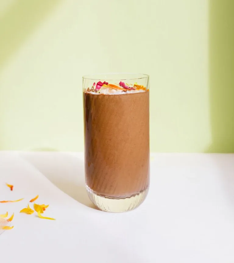 Glass of Metabolism Super Powder chocolate smoothies, topped with coconut flakes, beside a whole apricot.