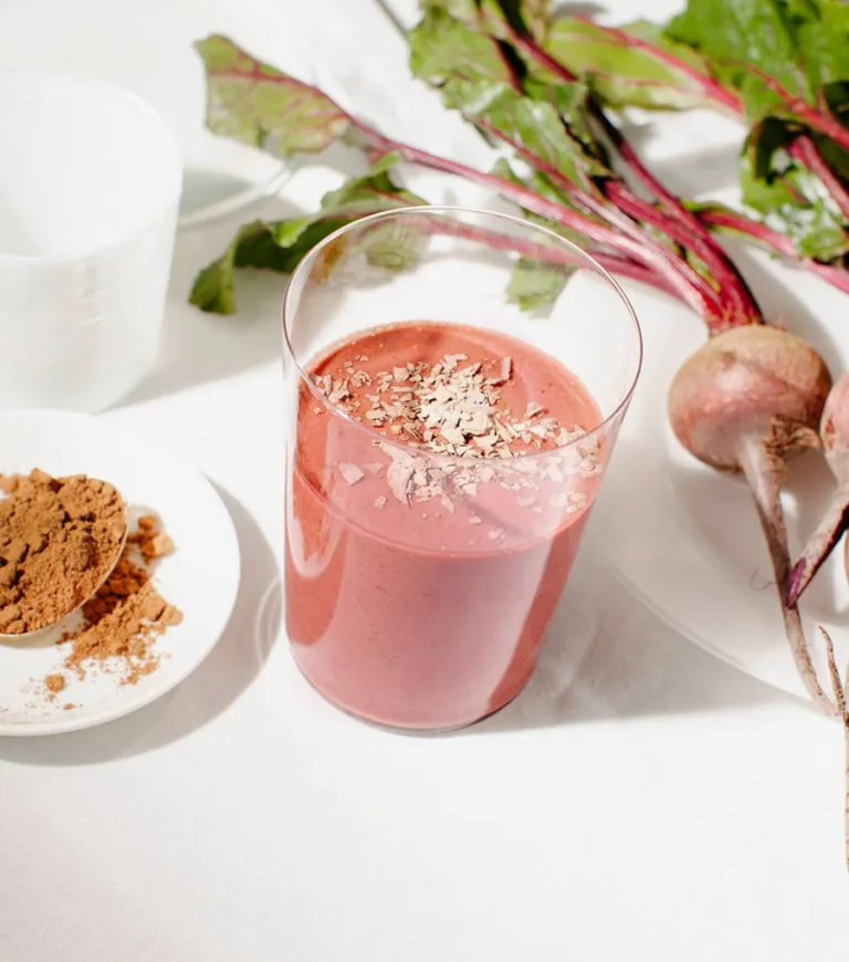 Red Velvet Metabolism Smoothie in a glass beside fresh beets and a small dish of Sakara Metabolism Super Powder.