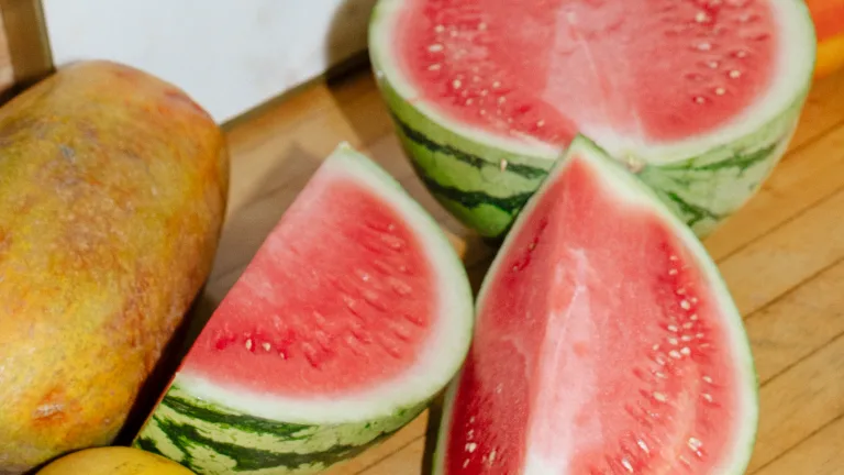 Sliced watermelon wedges and a whole papaya arranged on a wooden surface.