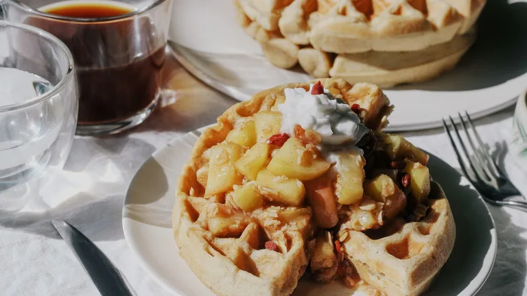 Plate of waffles topped with warm fruit compote and yogurt beside a glass of coffee.